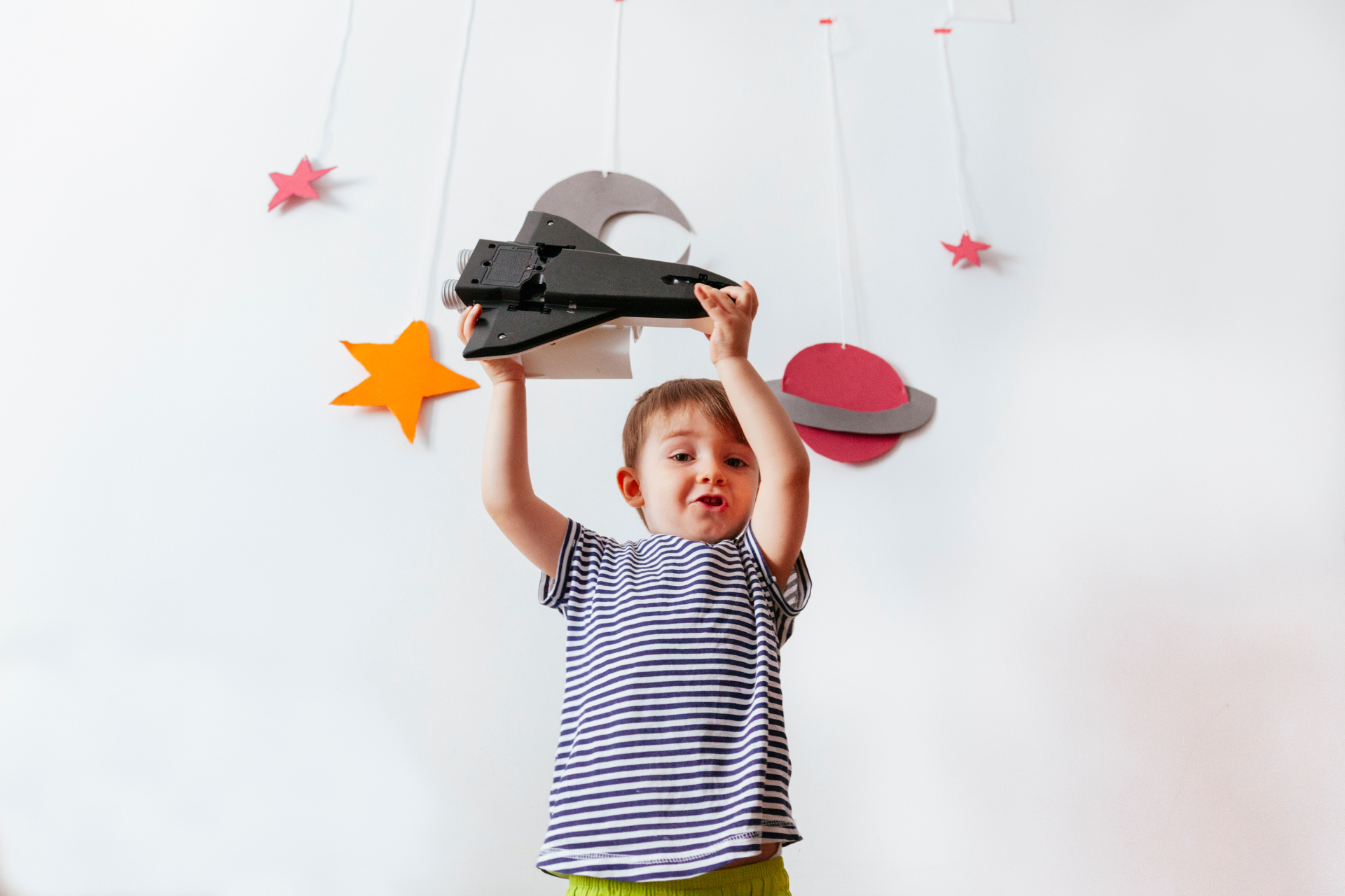 cute child playing with rocket toy in space-themed room